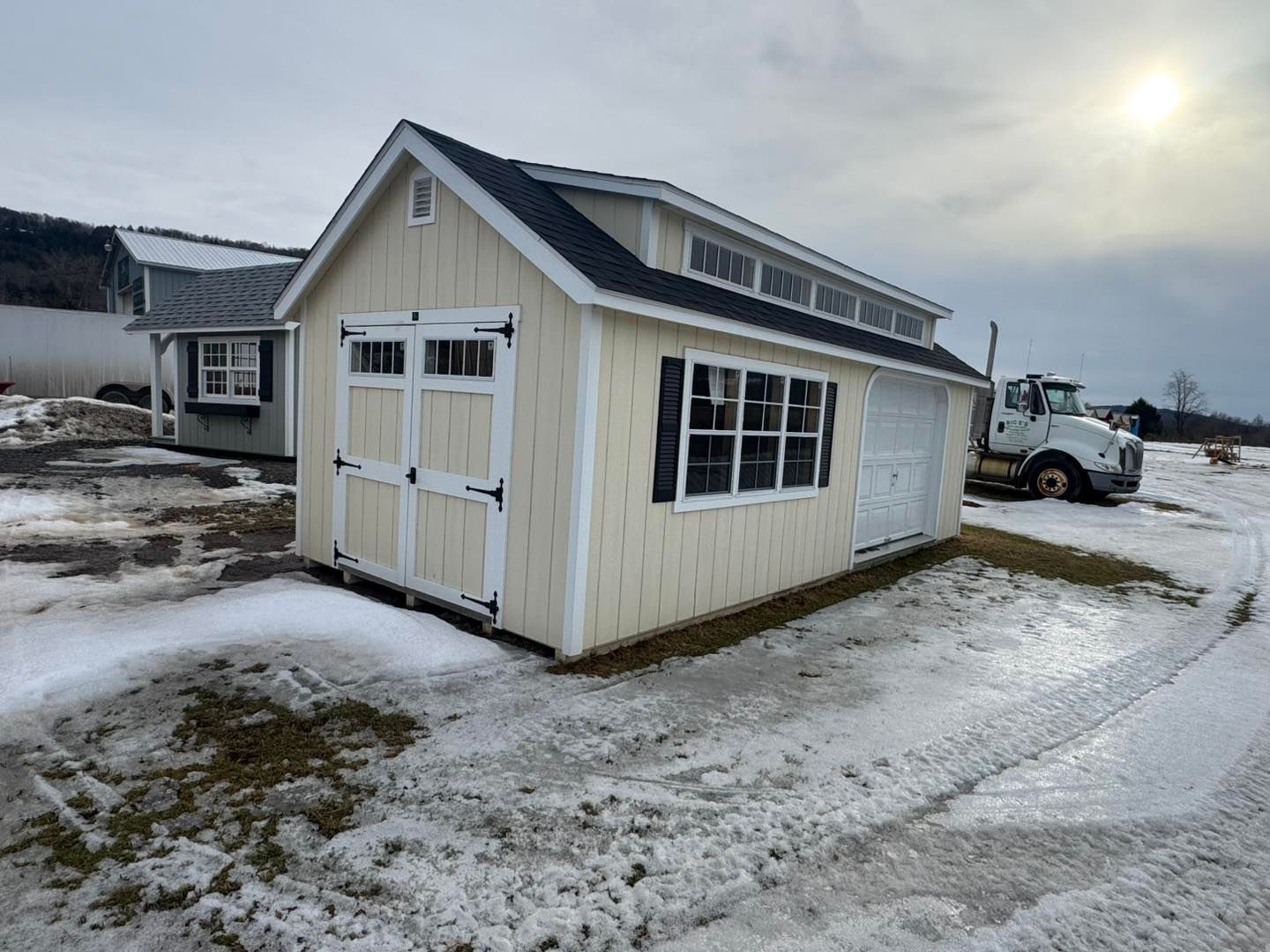 A shed with a garage attached to it is sitting in the snow next to a truck.