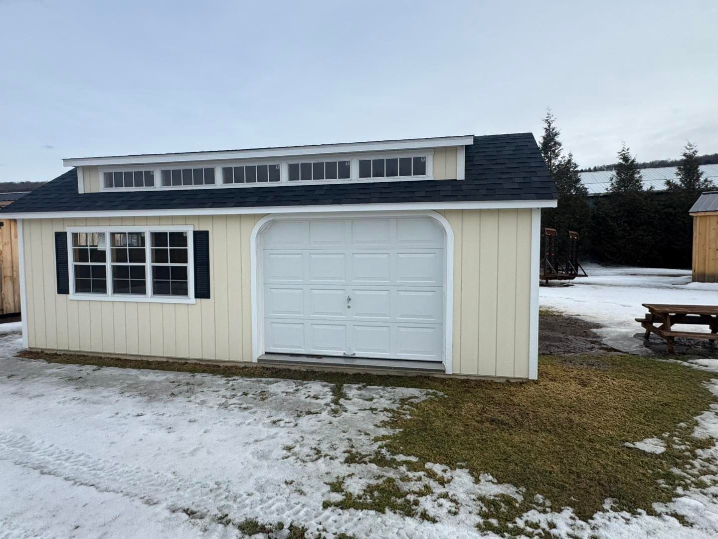 A white garage with a black roof is sitting in the snow.