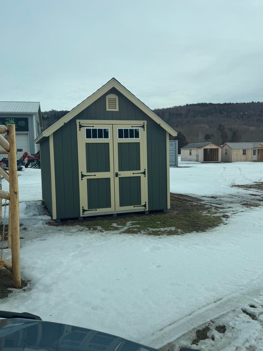 A green and white shed is sitting in the middle of a snowy field.
