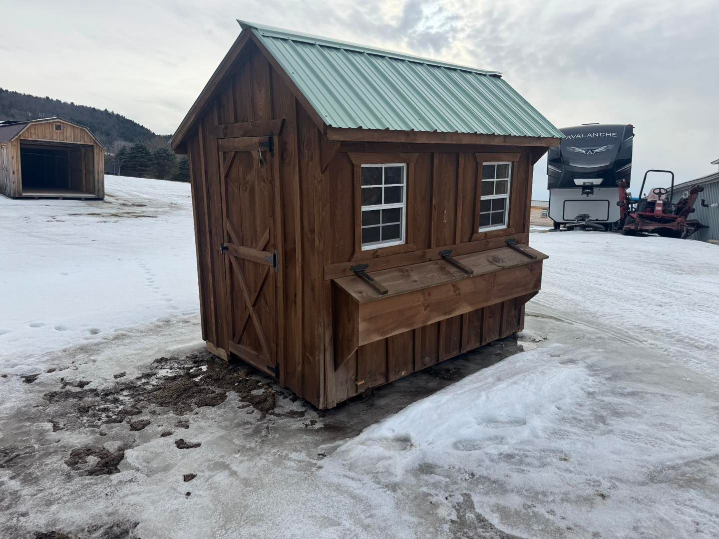 A small wooden shed with a green roof is sitting in the snow.