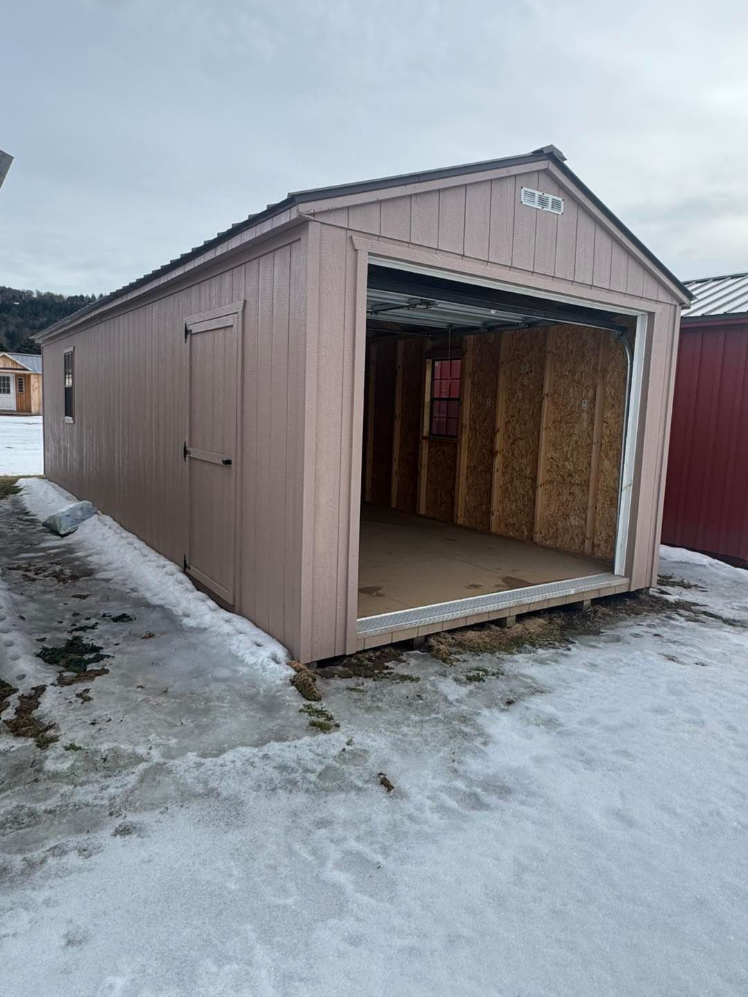 A shed with the door open is sitting in the snow.