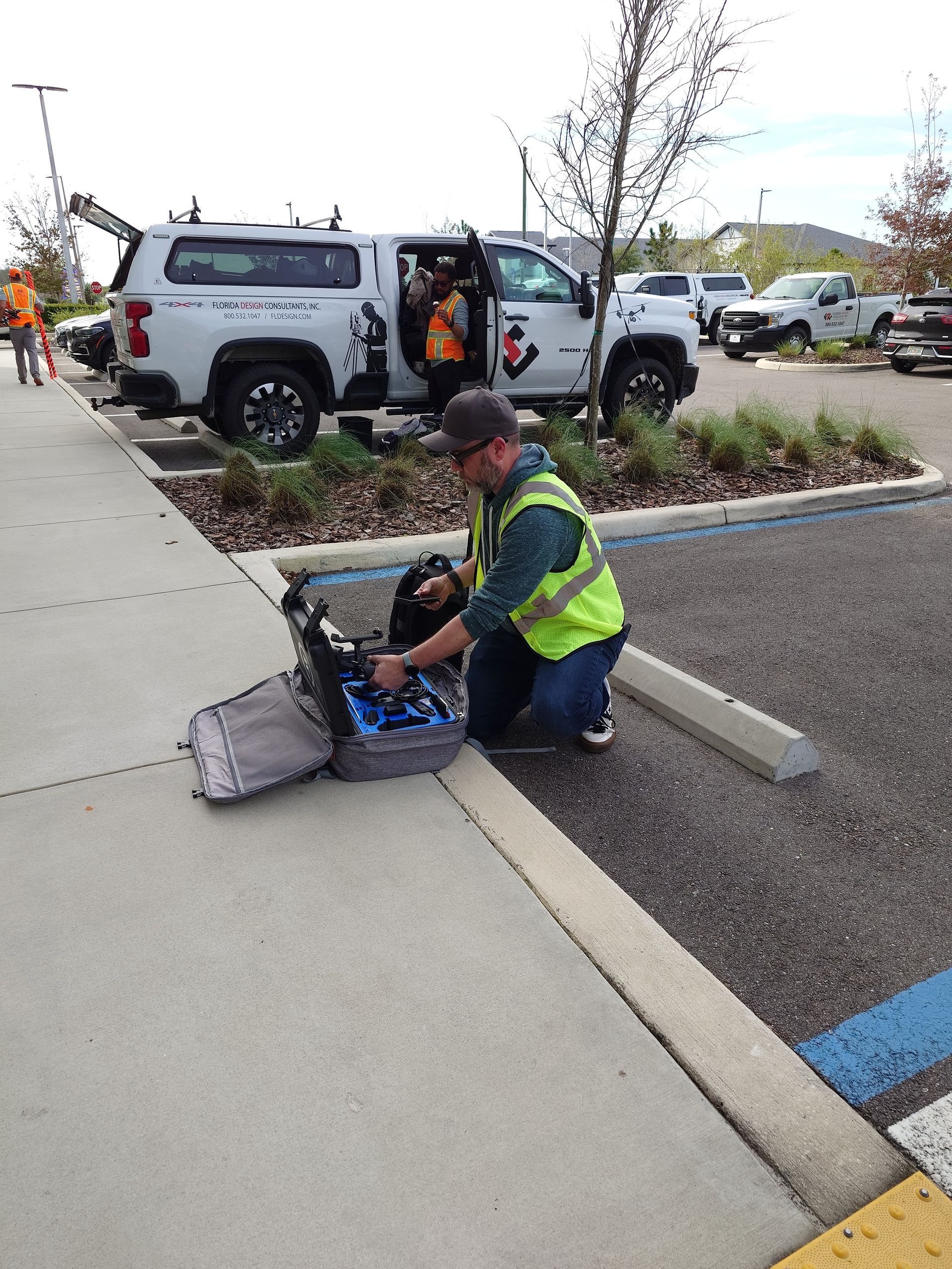 Worker in reflective vest operating a tool beside a gray utility truck in a parking lot.