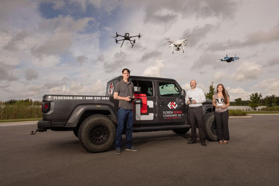A group of people standing next to a truck with drones flying in the background.