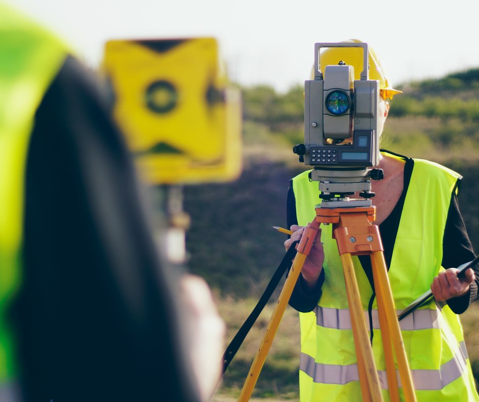 A man in a yellow vest is using a theodolite on a tripod to survey land