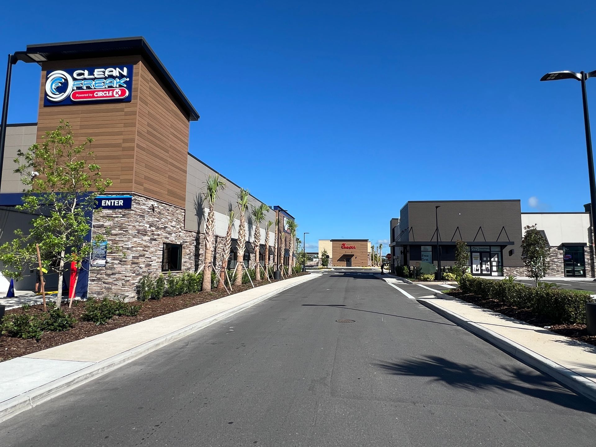A car wash and storefronts line a street under a clear blue sky.