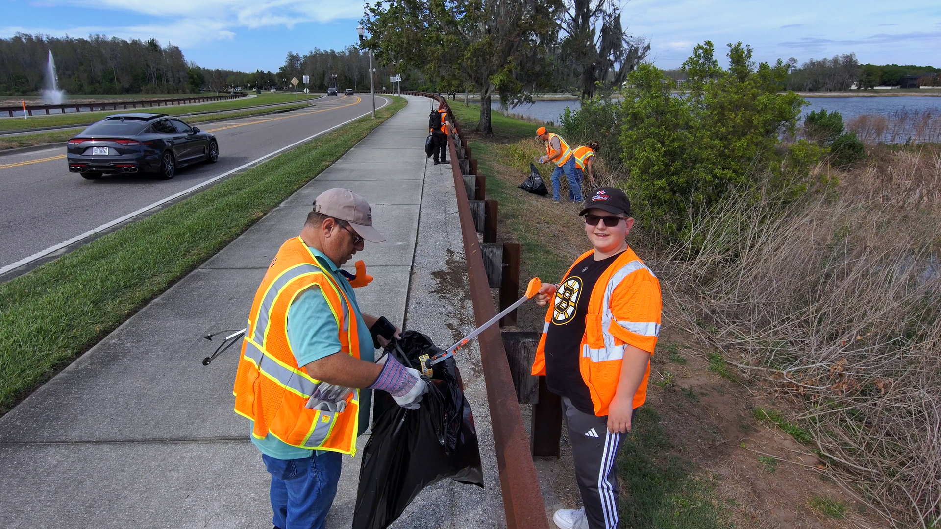 Workers in orange vests clearing debris from a roadside drainage ditch