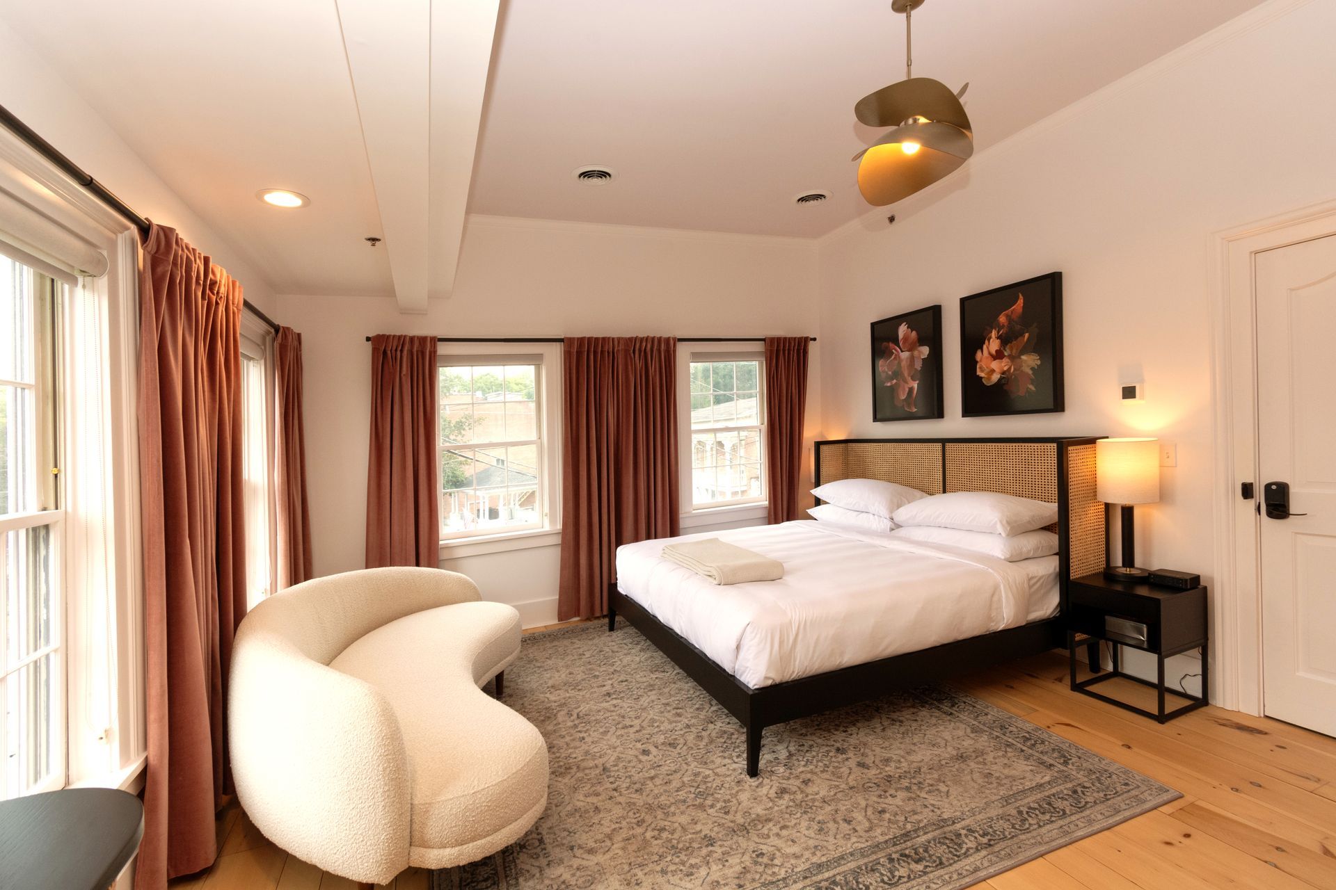 Picture of the room called Herrick featuring a king bed with four windows flanked with long pink drapes and a large white couch.
