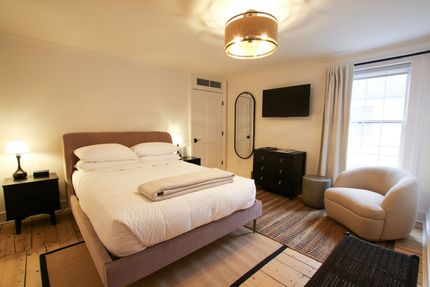 A medium size room with queen size bed and one window draped by white velvet curtains. A pendant light hangs over the bed.
