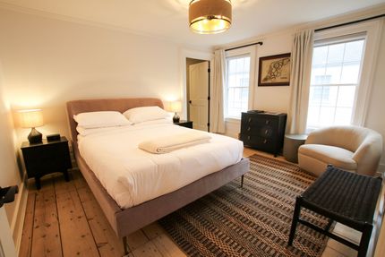 A medium size room with queen size bed and two windows draped by white velvet curtains. A pendant light hangs over the bed.