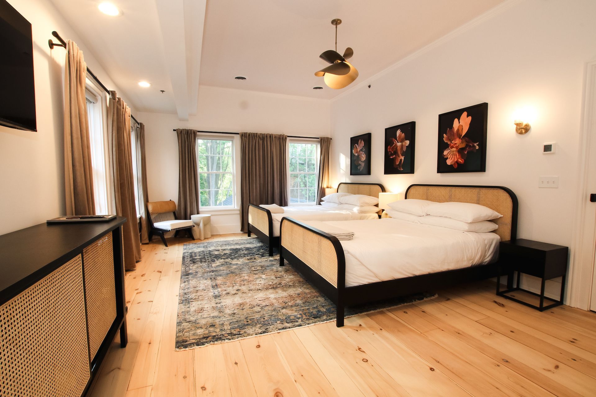 Picture of the room called Roberts featuring two queen beds with four windows flanked with long neutral colored drapes. A blue rug lies below the beds and chair sits in the corner.