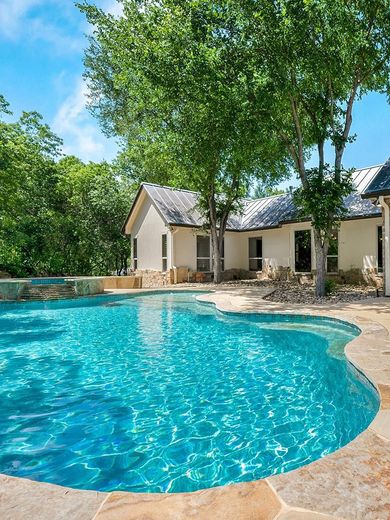 A large swimming pool in front of a house surrounded by trees.