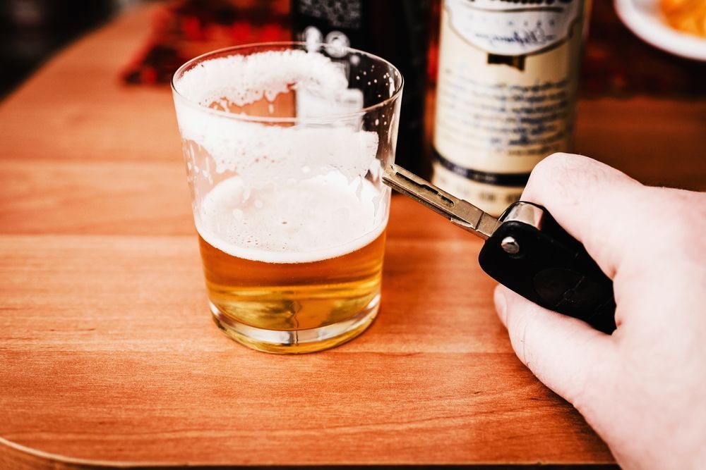 A person is holding a car key next to a glass of beer.