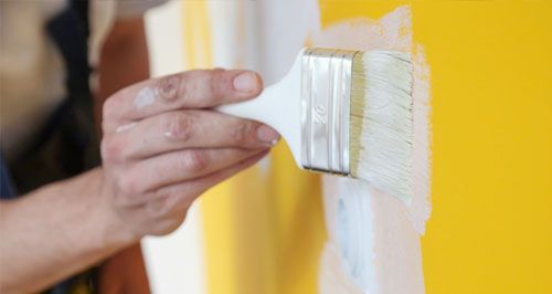 Una persona está pintando una pared amarilla con un pincel blanco.
