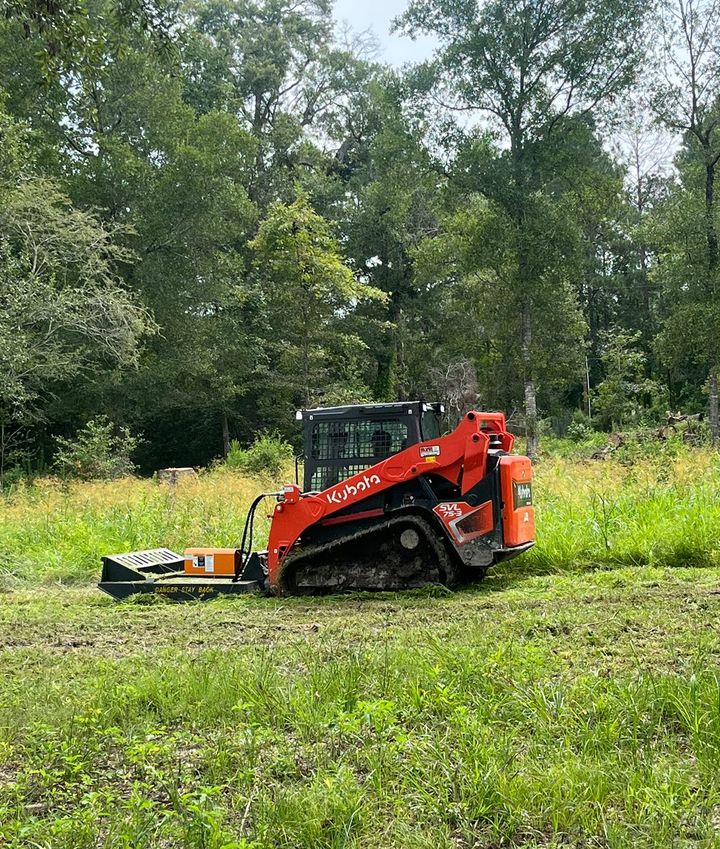 A bulldozer is cutting grass in a field with trees in the background.