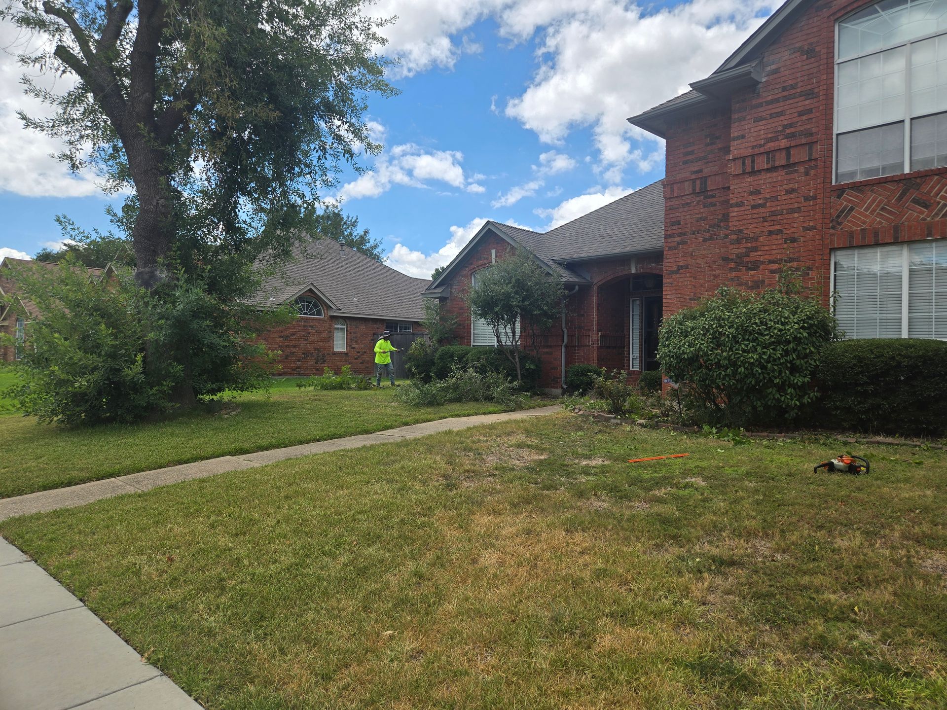 Hedges and bushes being trimmed in front of a brick house.