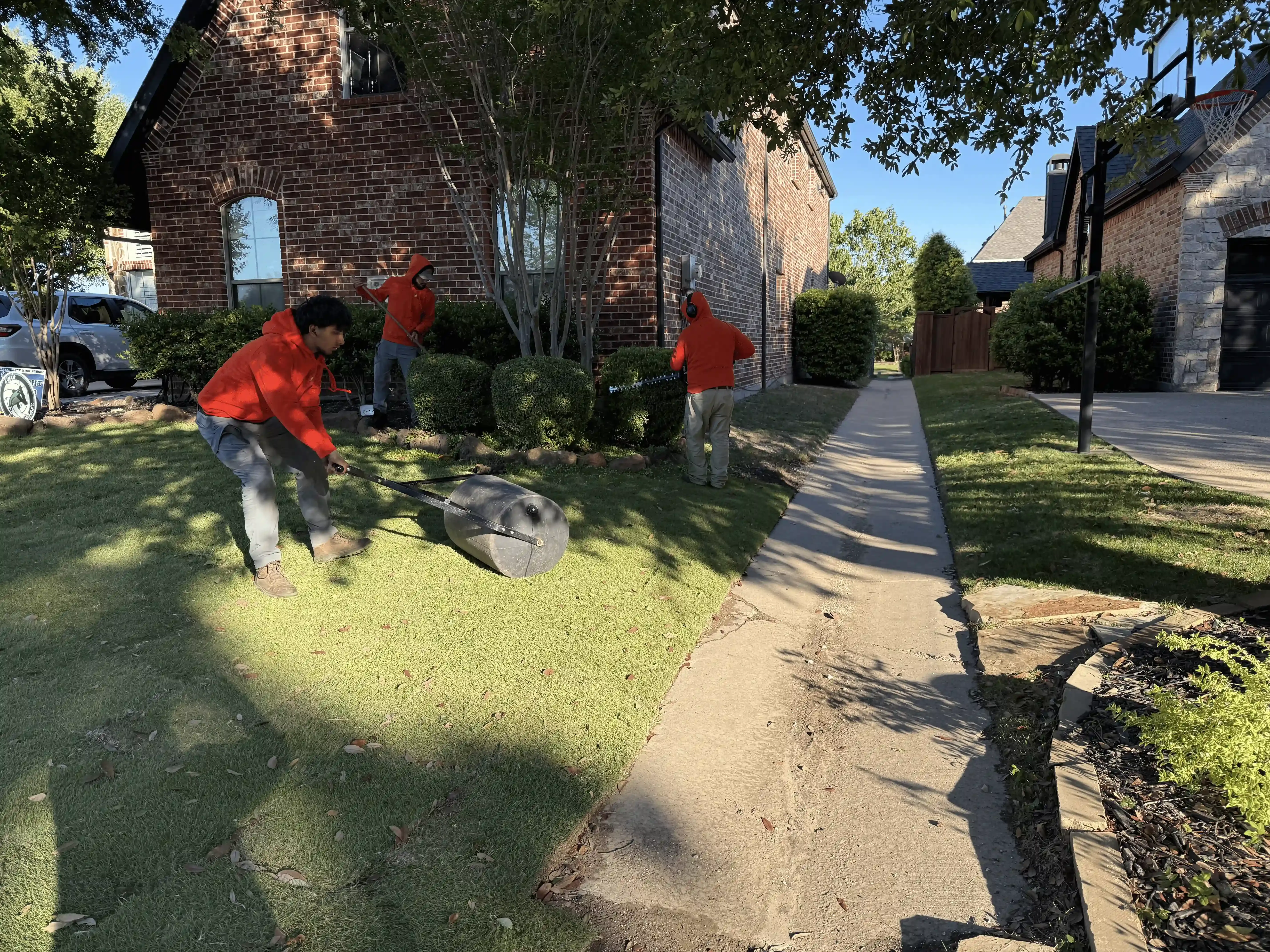 A group of people are cutting grass in front of a house.