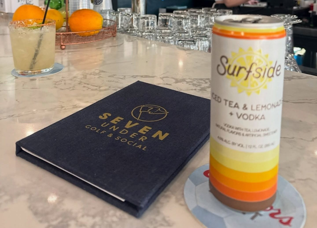 Bartender pouring cocktails into glasses on a bar. Yellow drink, tattoos visible.