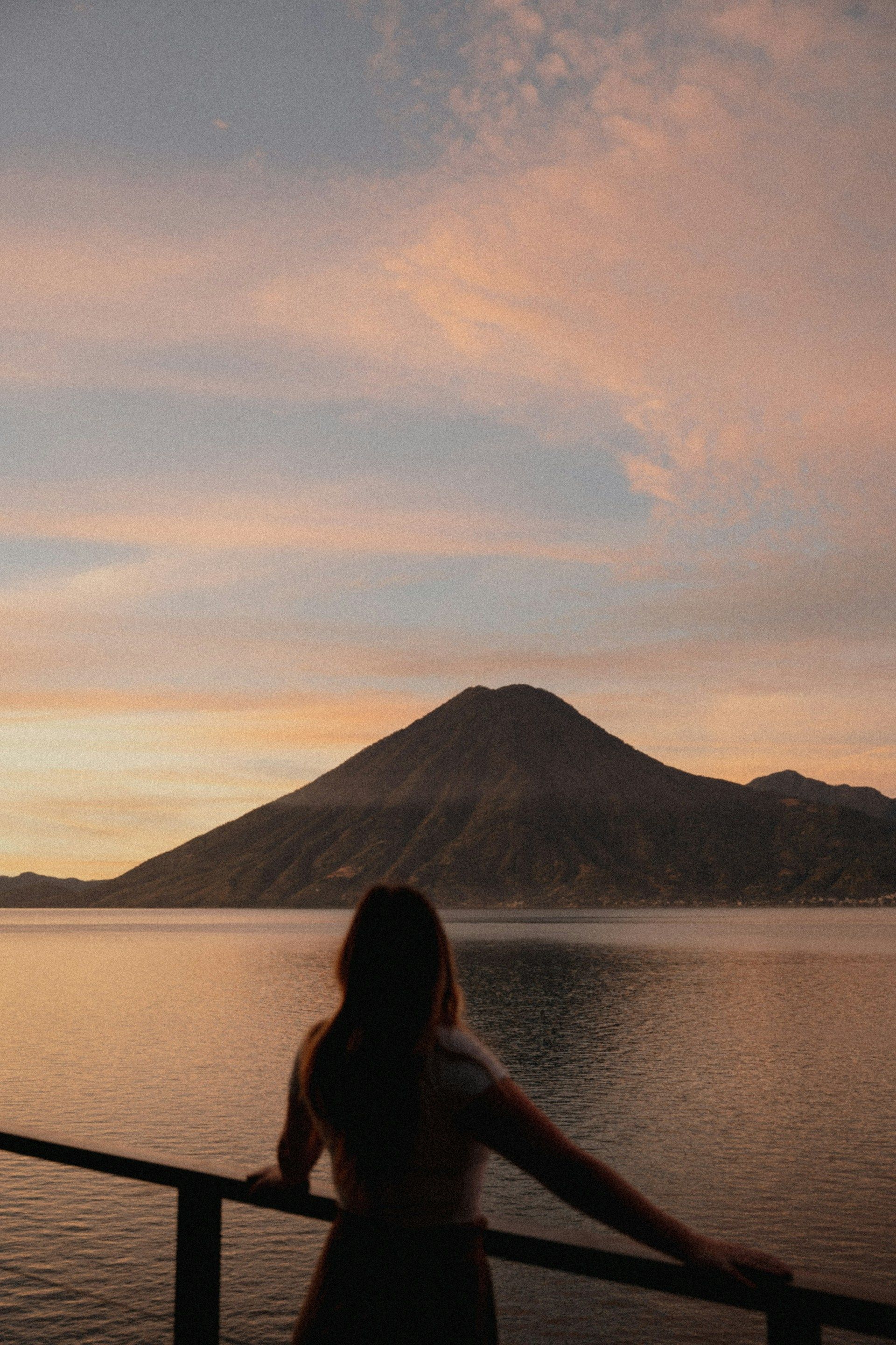 Una mujer está parada en un muelle con vistas a un lago al atardecer.