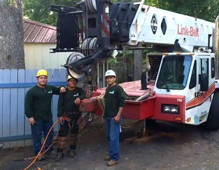 Three workers stand beside a red and white Link-Belt crane on a street.
