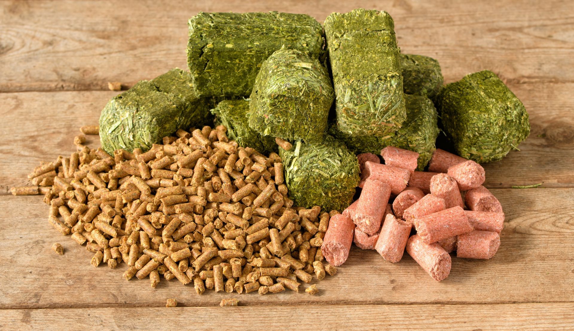 Green, brown, and pink pet food pellets arranged on a wooden surface