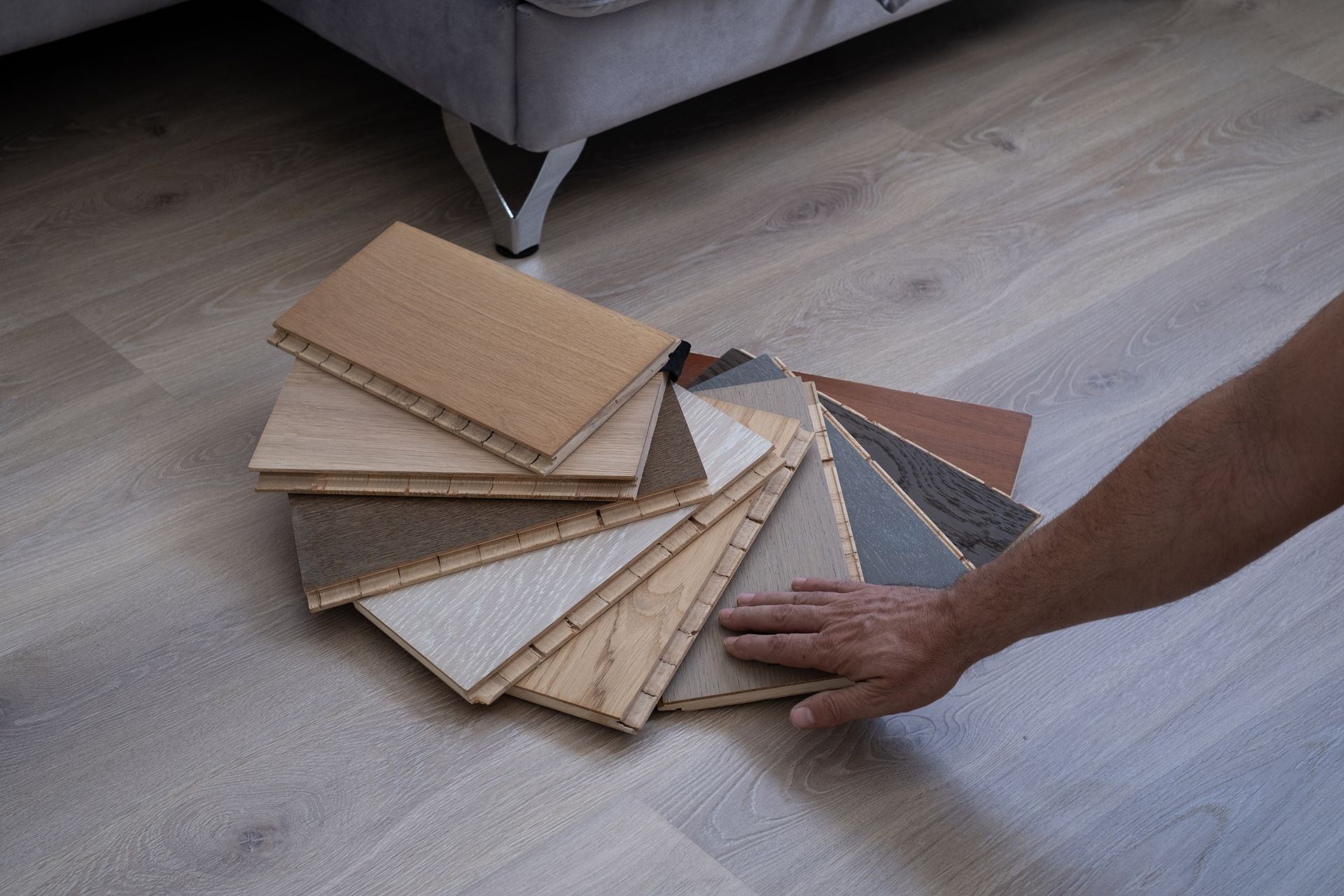 A person choosing from wooden flooring samples laid out on a floor in natural daylight