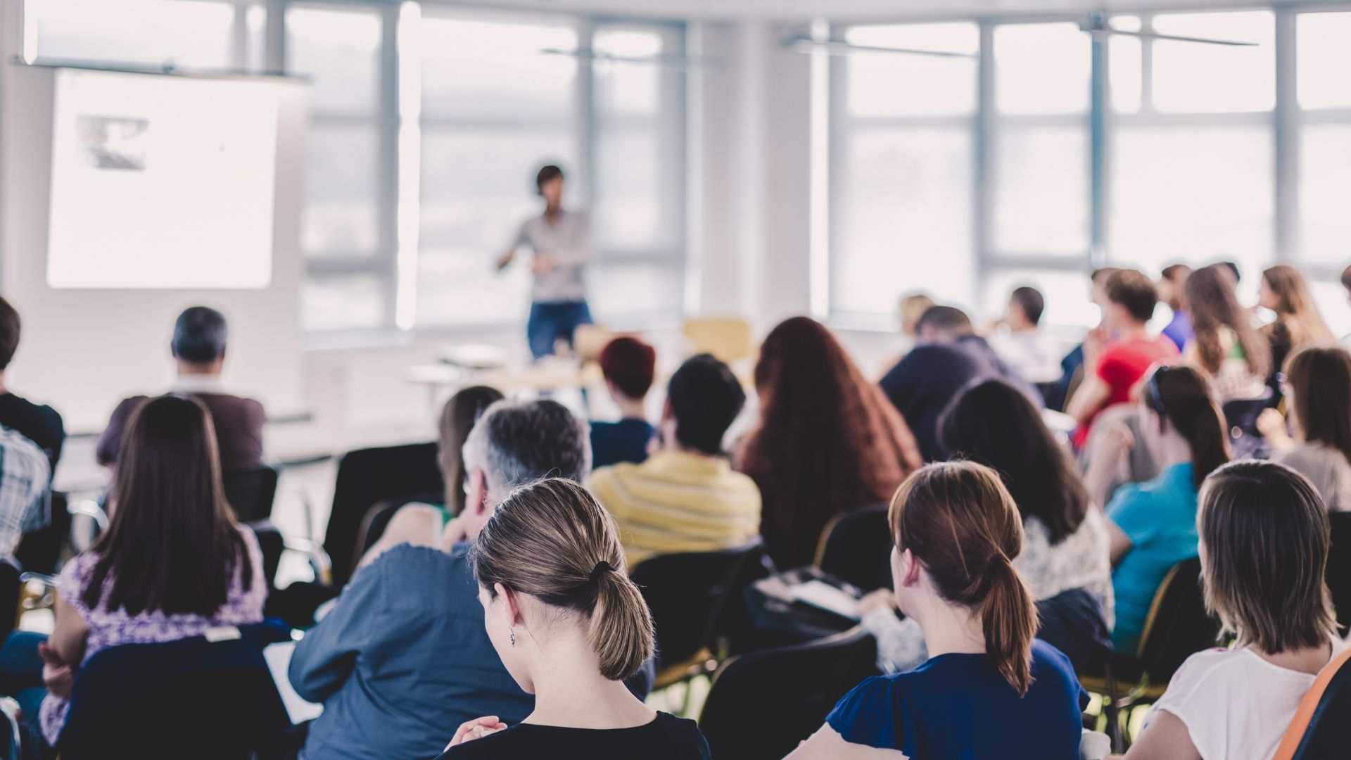 A group of people are sitting in a lecture hall watching a presentation.