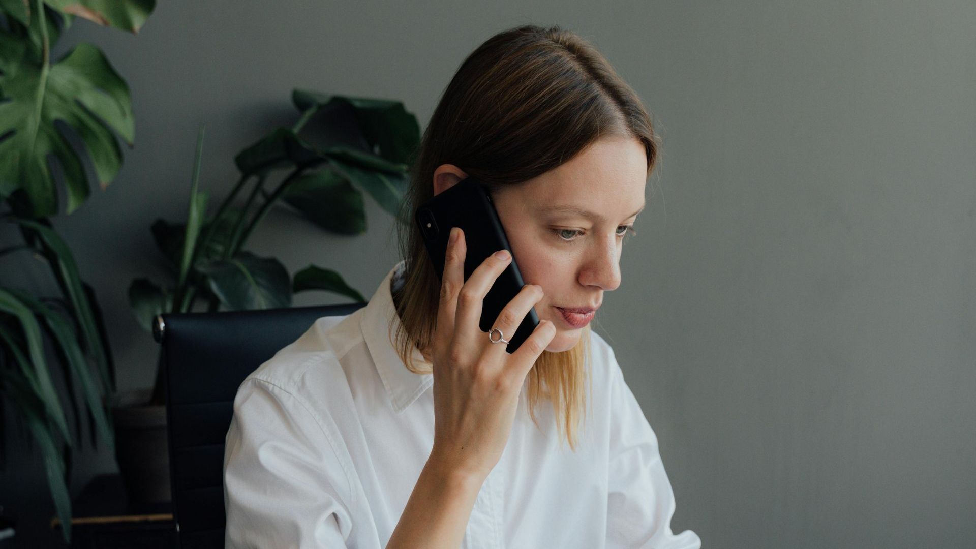A woman is sitting at a desk talking on a cell phone.