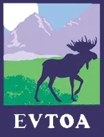 A moose is standing in a field with mountains in the background.