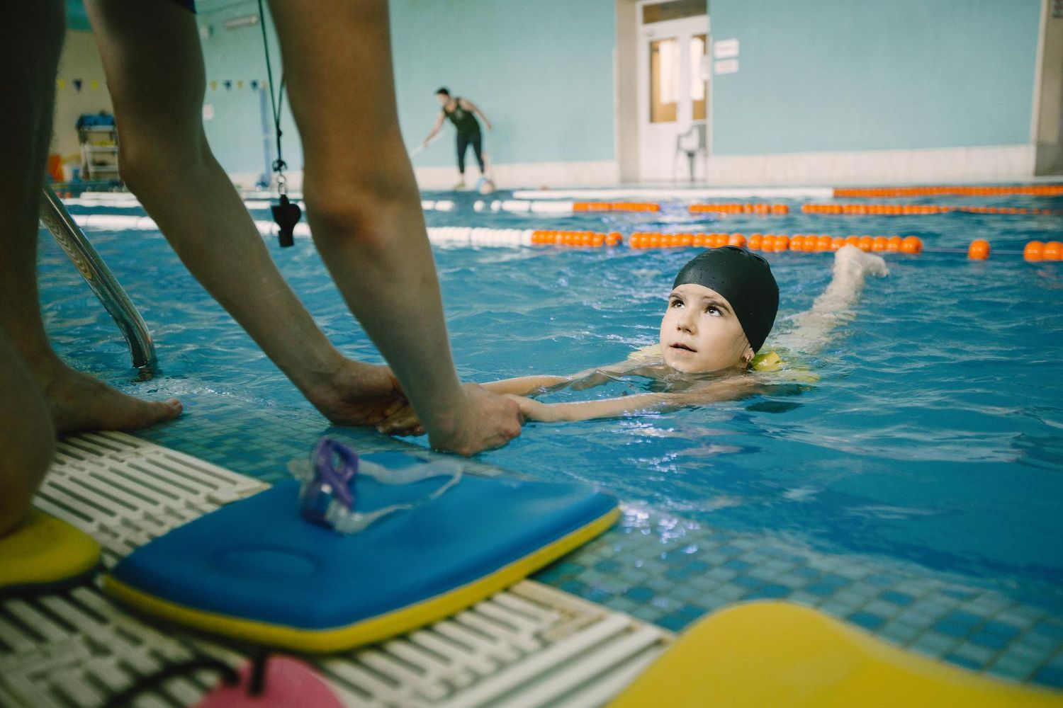 Coach teaching kid in indoor swimming pool how to swim and dive