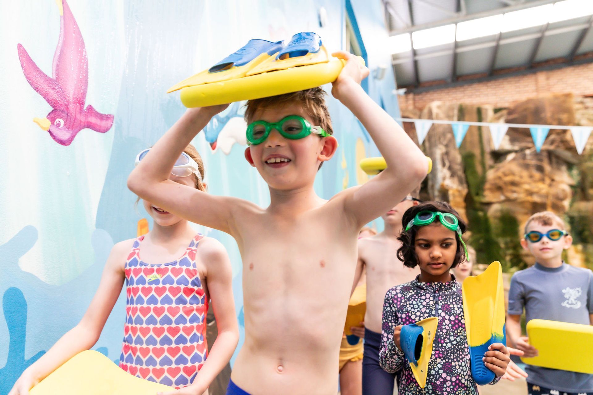 Children wearing colorful swim goggles and holding pool toys at an outdoor water activity event