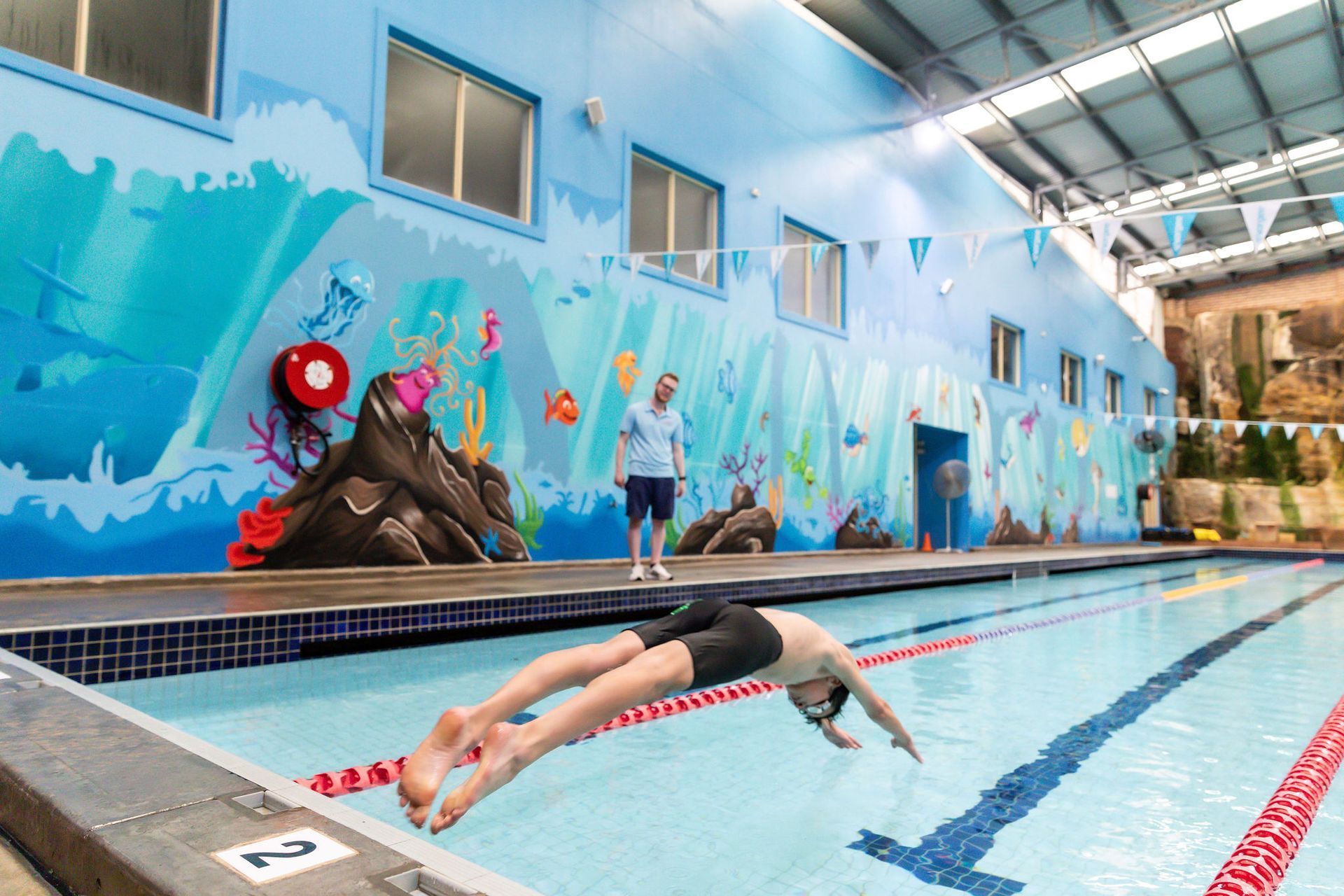 Swimmer gliding in an outdoor pool beside a blue mural wall