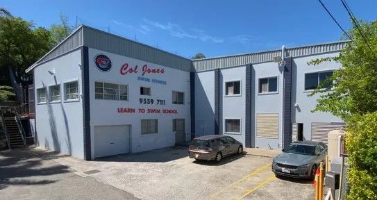 A two-story light gray Cal Jones Diving School building with a parked minivan and SUV on a concrete lot under blue sky.