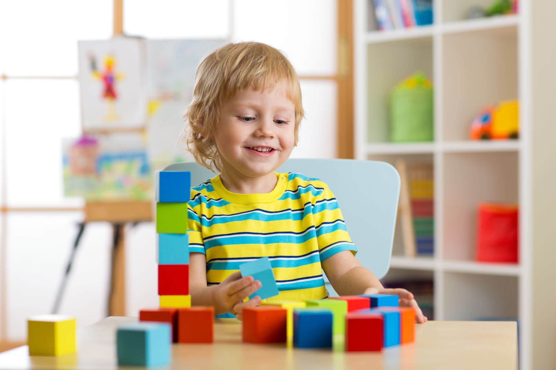 Boy smiles while playing with colorful building blocks on a table indoors.