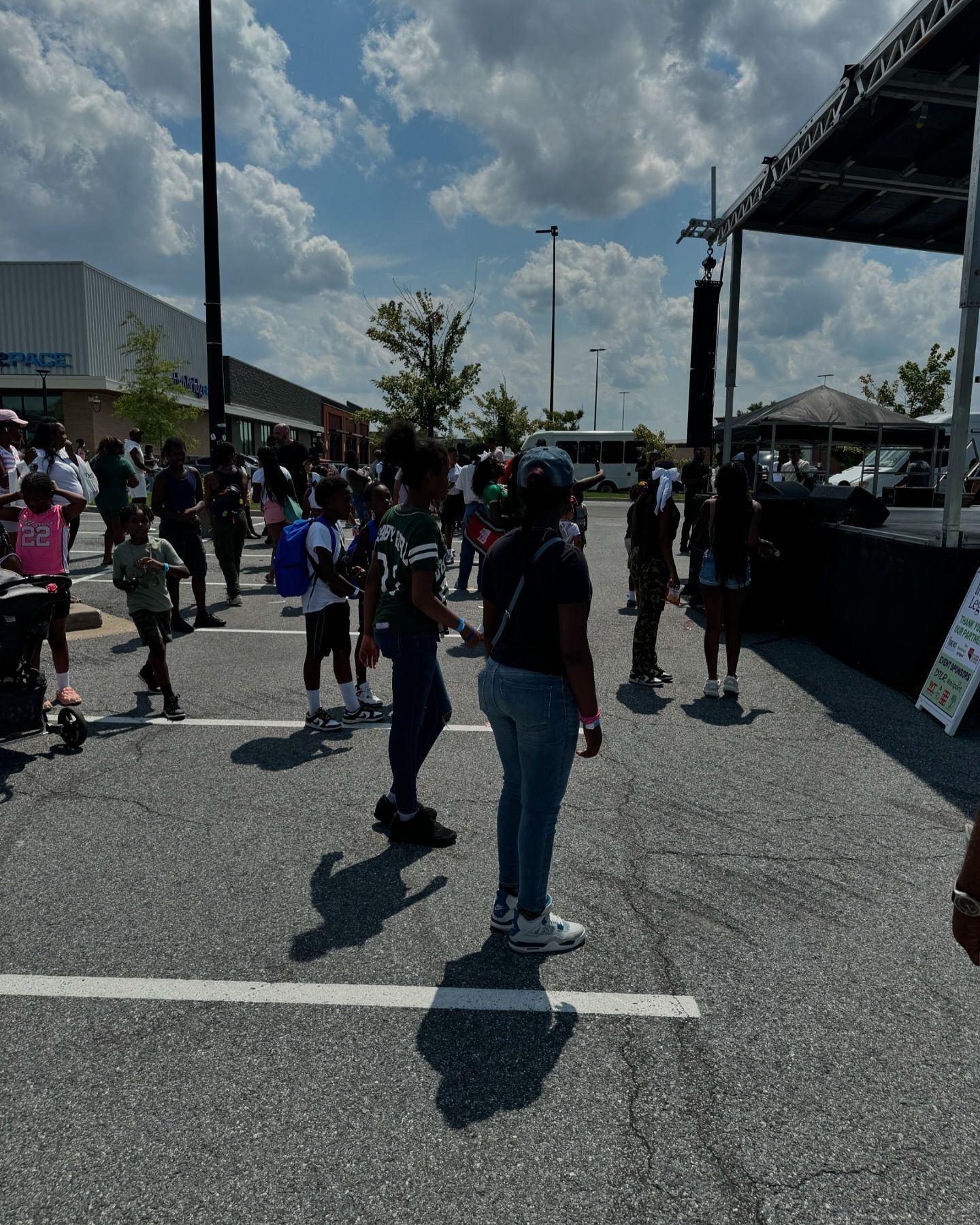 People gathered outside near a stage on a sunny day.