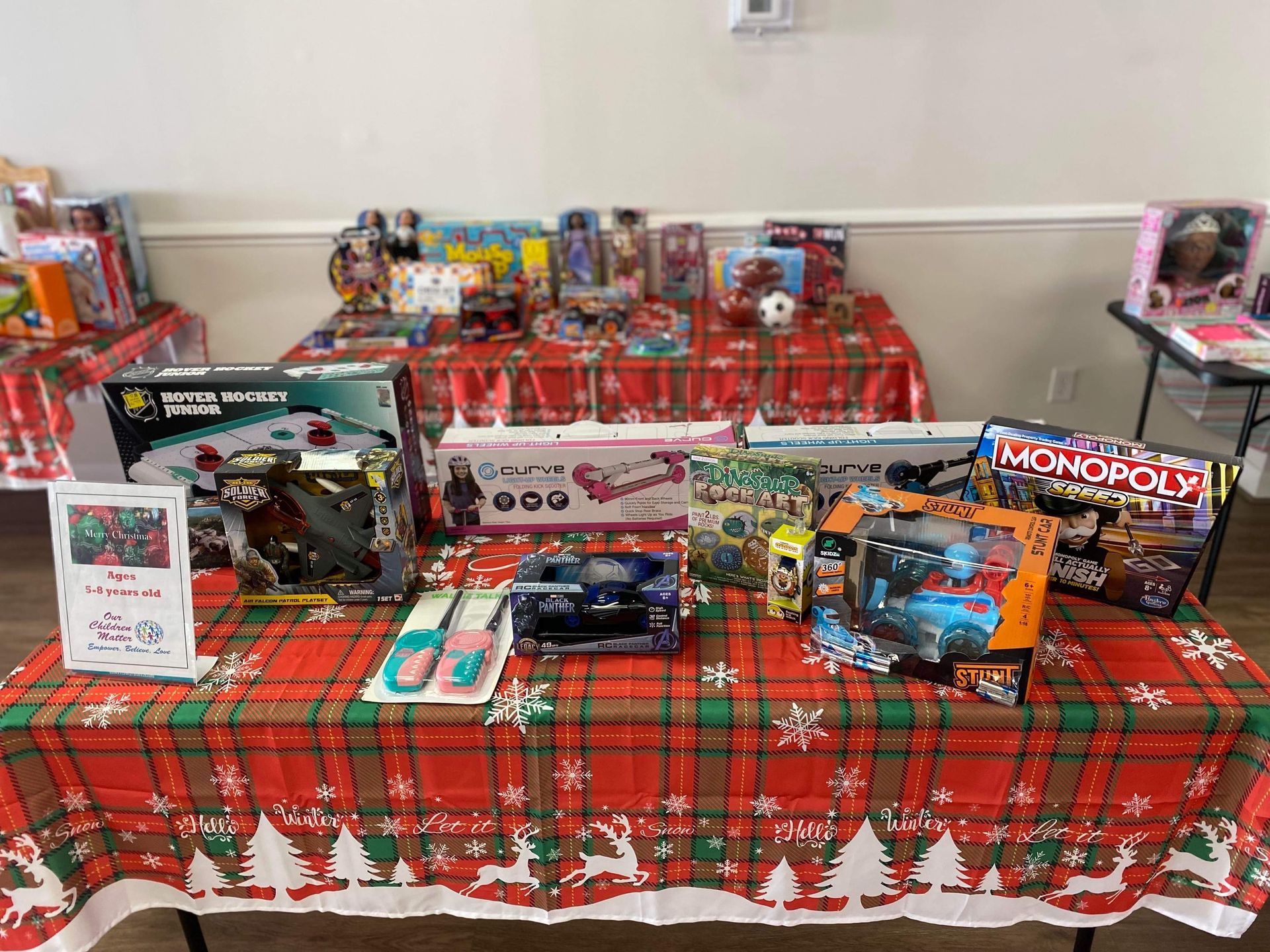Table laden with toys, decorated with red and green Christmas tablecloths, for a holiday giveaway.