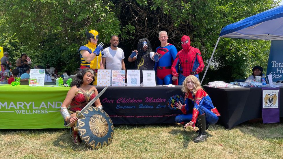People in superhero costumes at a booth with a 