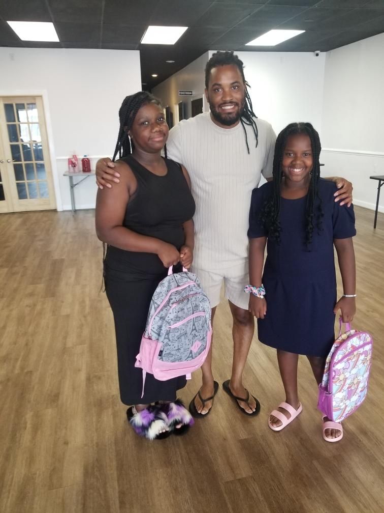 Family posing for a photo indoors, each holding a backpack.