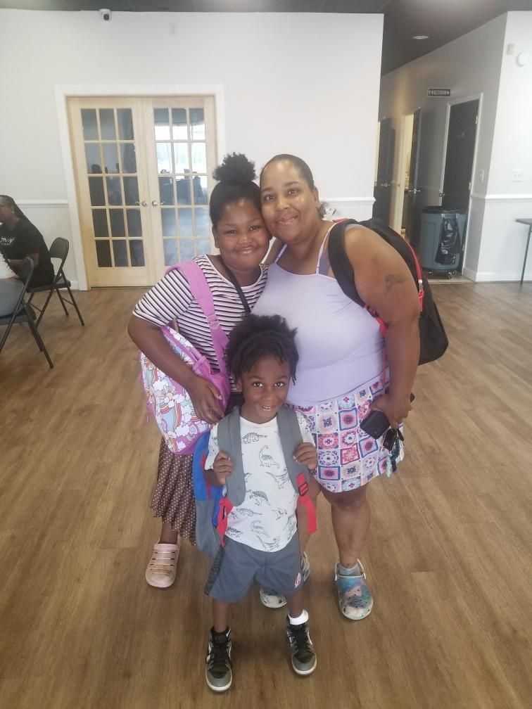 Three people pose with backpacks in a room: one adult, a teen, and a child.