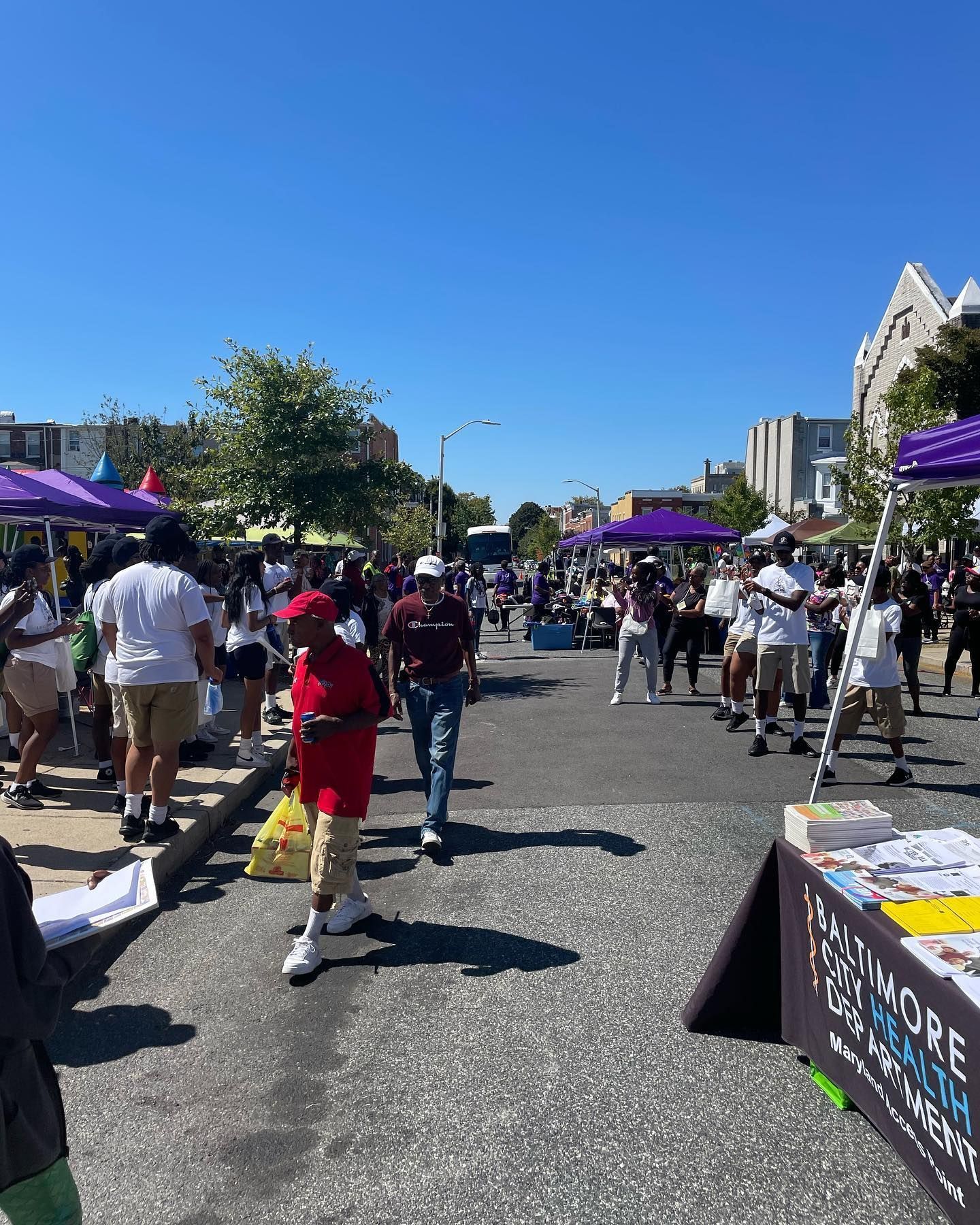 Street fair with purple tents and many people on a sunny day.