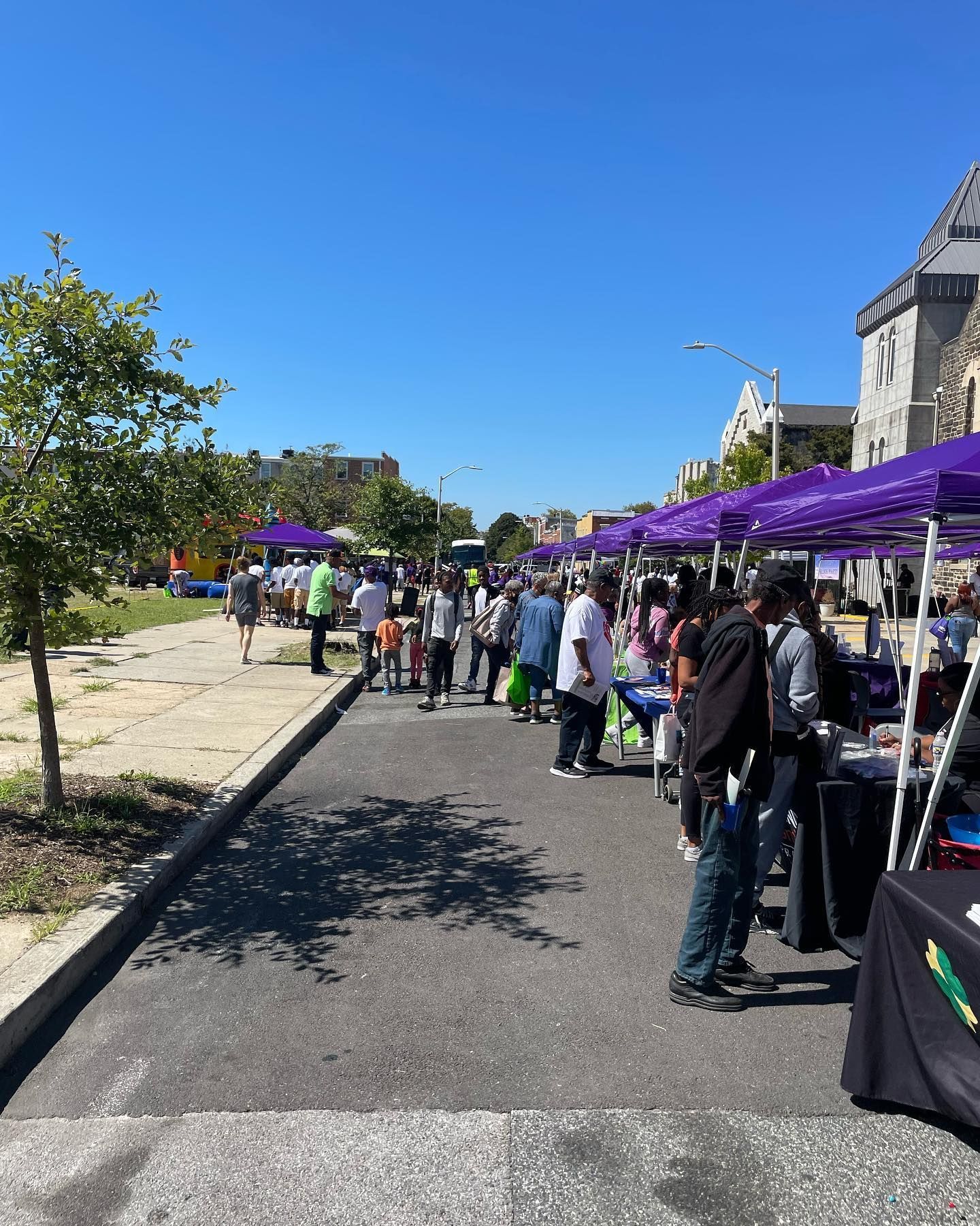 Street fair with purple tents, people walking, sunny day.