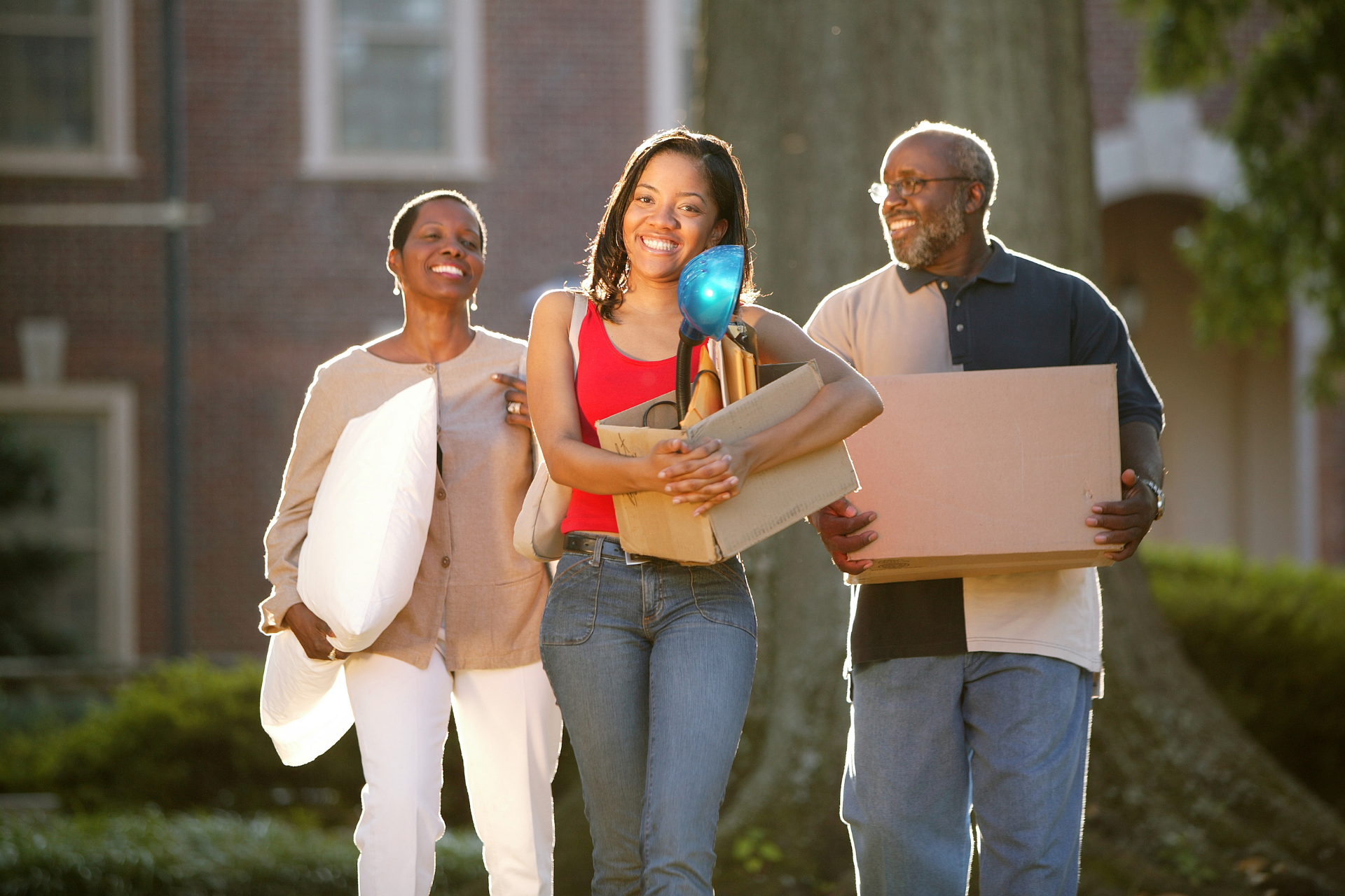 Family moving daughter into college; they carry boxes and belongings outdoors.