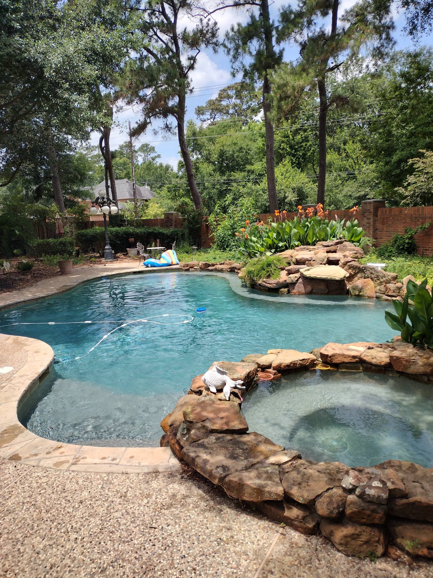 Backyard pool with a stone hot tub, rock waterfall, and trees in the background