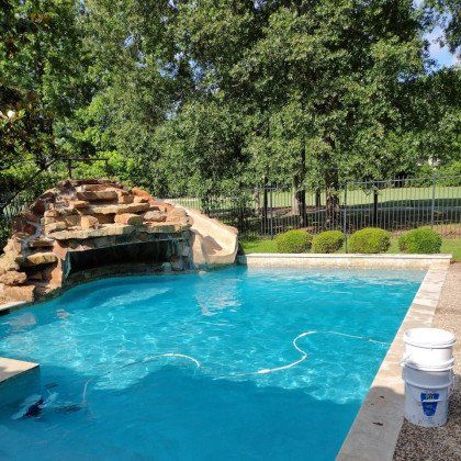 Backyard pool with a rock waterfall, trees, and a white bucket on the deck