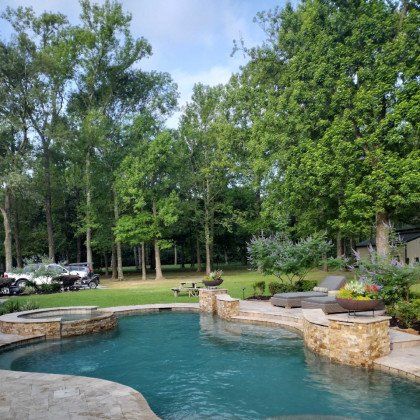 Backyard pool with turquoise water, stone seating, and a wooded lawn backdrop