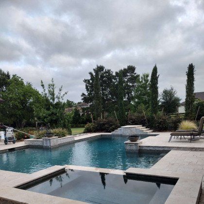 Backyard pool with stone patio, lounge chairs, and cloudy sky