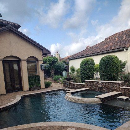 Courtyard with a swimming pool, stone spa, and beige houses under a partly cloudy sky