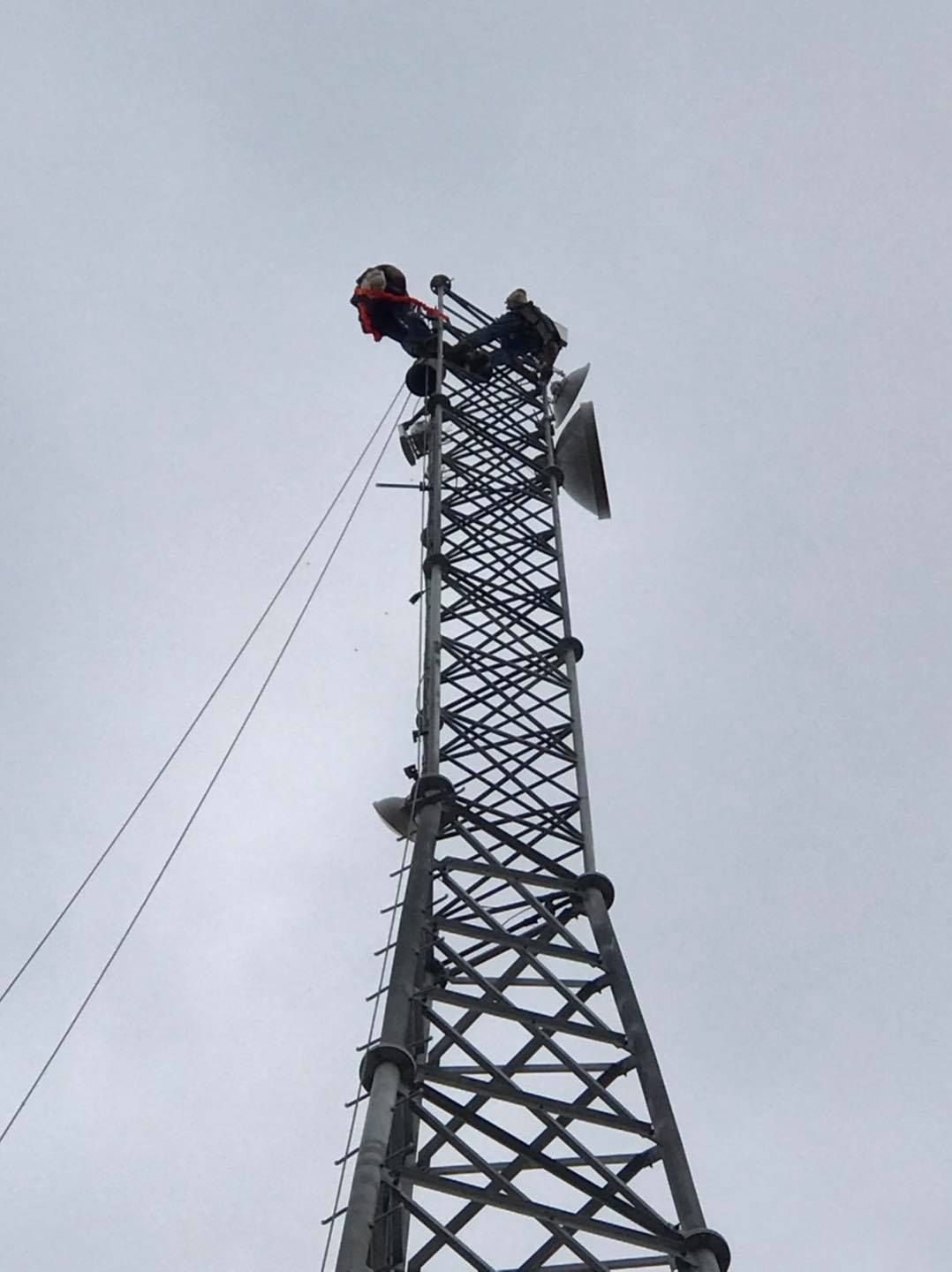 A worker on a tall communication tower, cloudy sky backdrop.