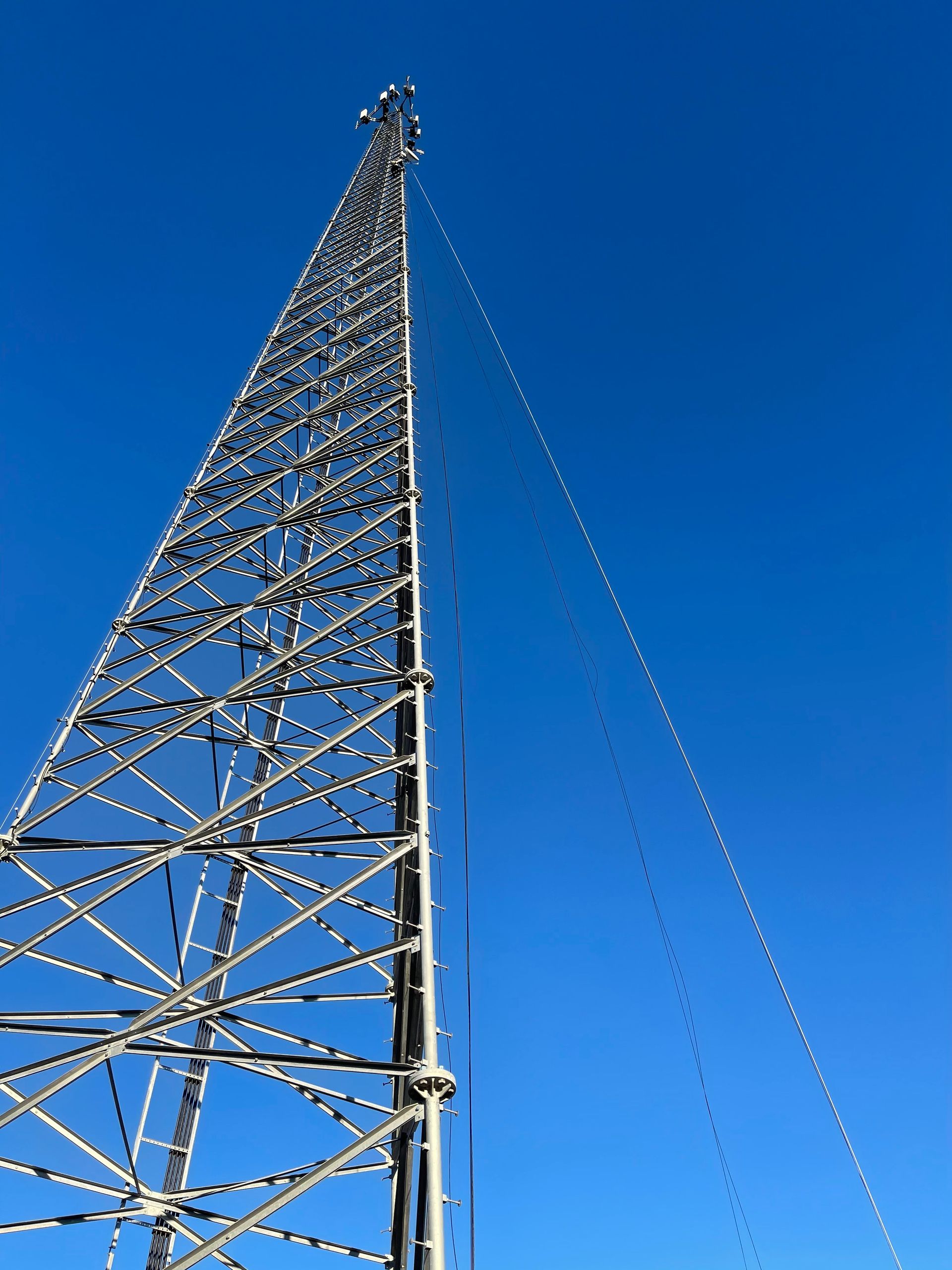 Steel lattice radio tower against a clear, blue sky. Guy wires extend from the tower.