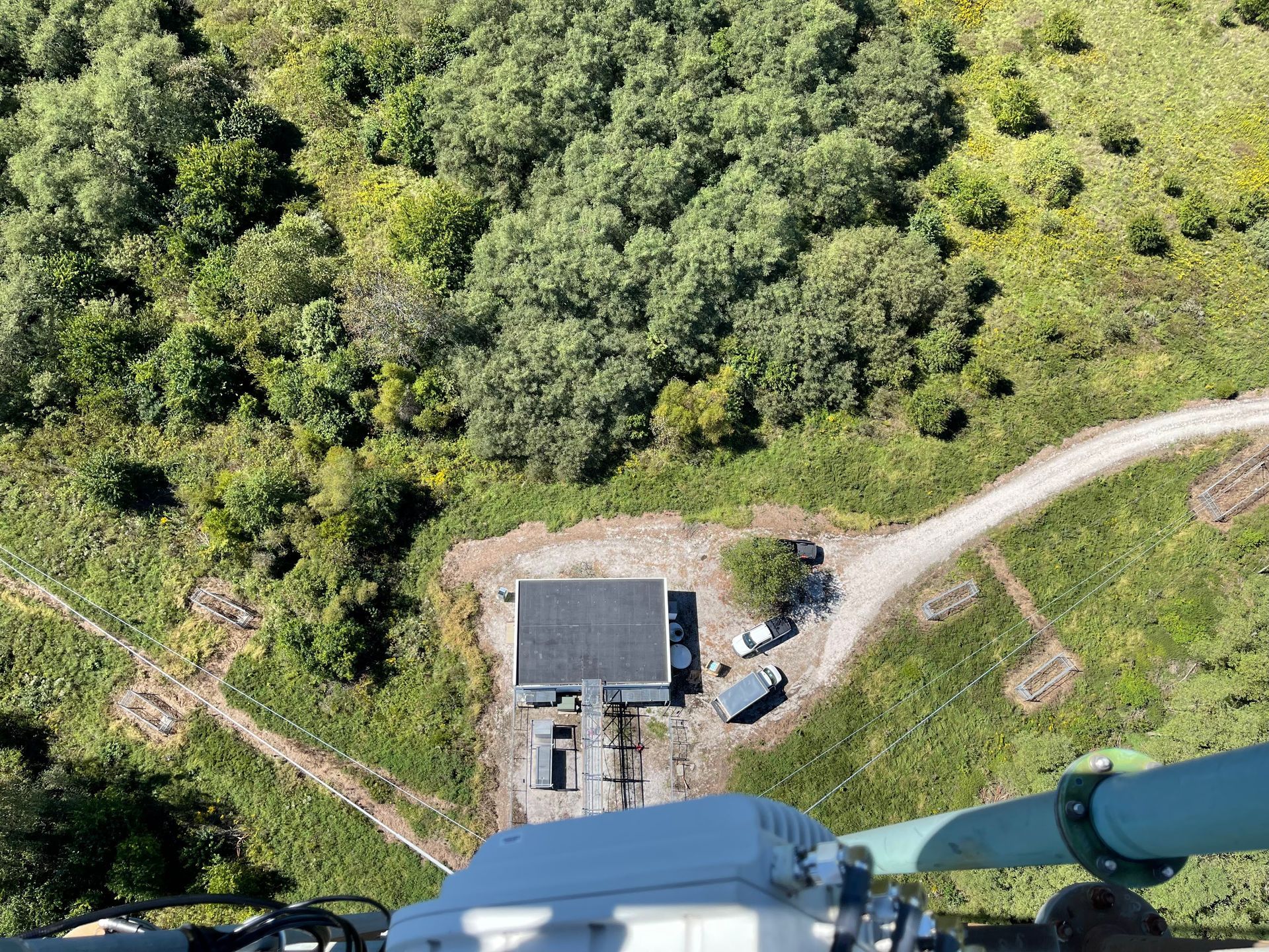 Overhead view of a small building, vehicles, and a gravel road surrounded by green trees and grass.