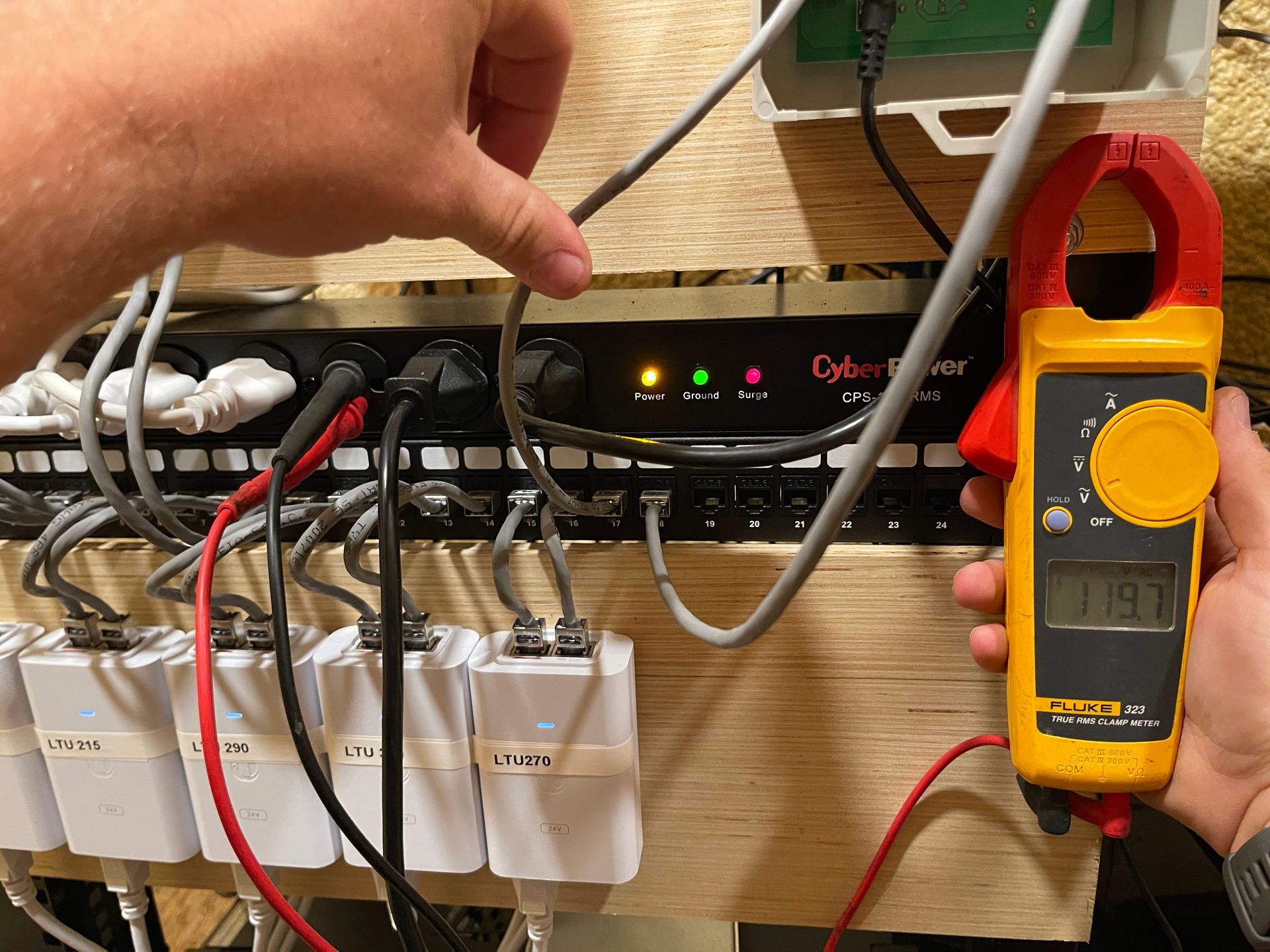 Person using a clamp meter to measure current in a power cable connected to a power distribution unit.